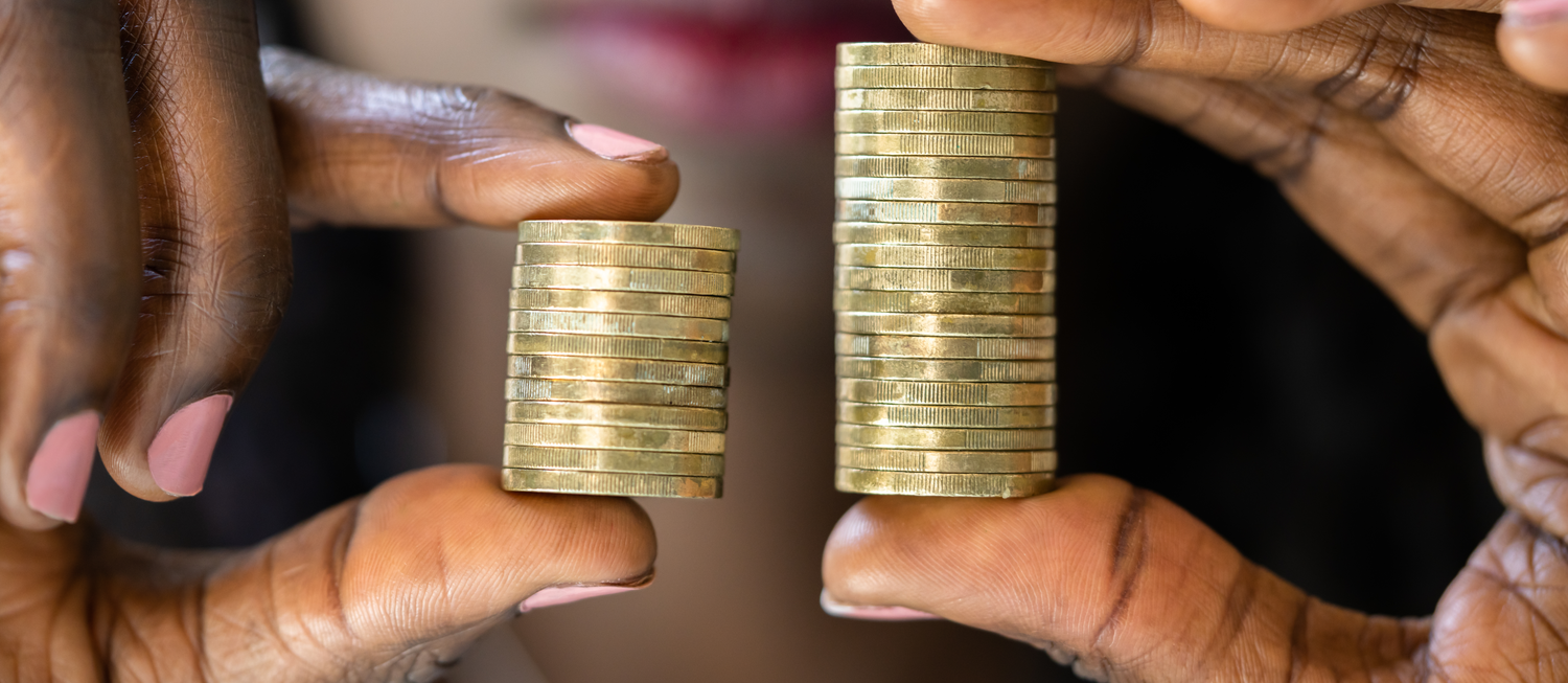 Photo of a person with dark skin holding two stacks of gold coins. One stack is half the size of the other stack.